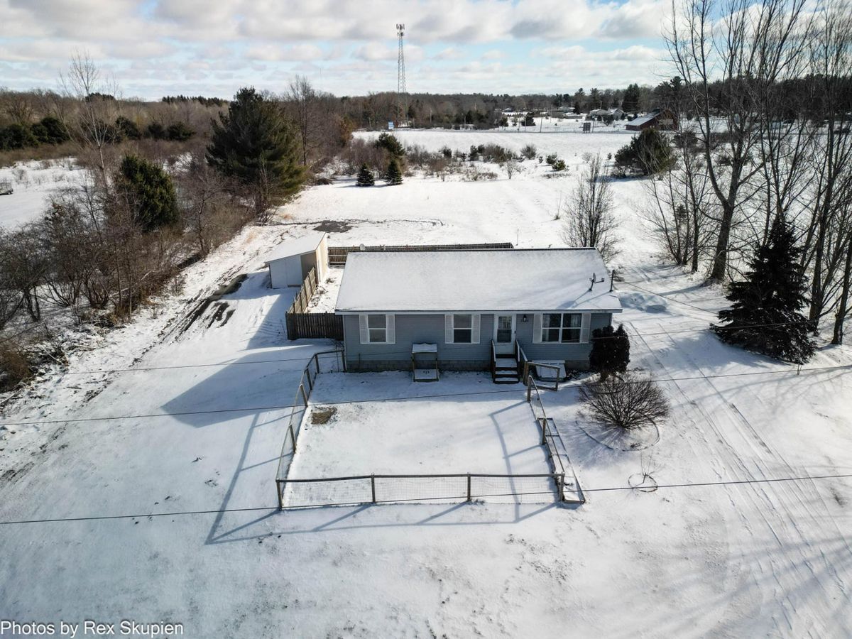 Aerial view of a gray ranch home on open acreage in winter snow