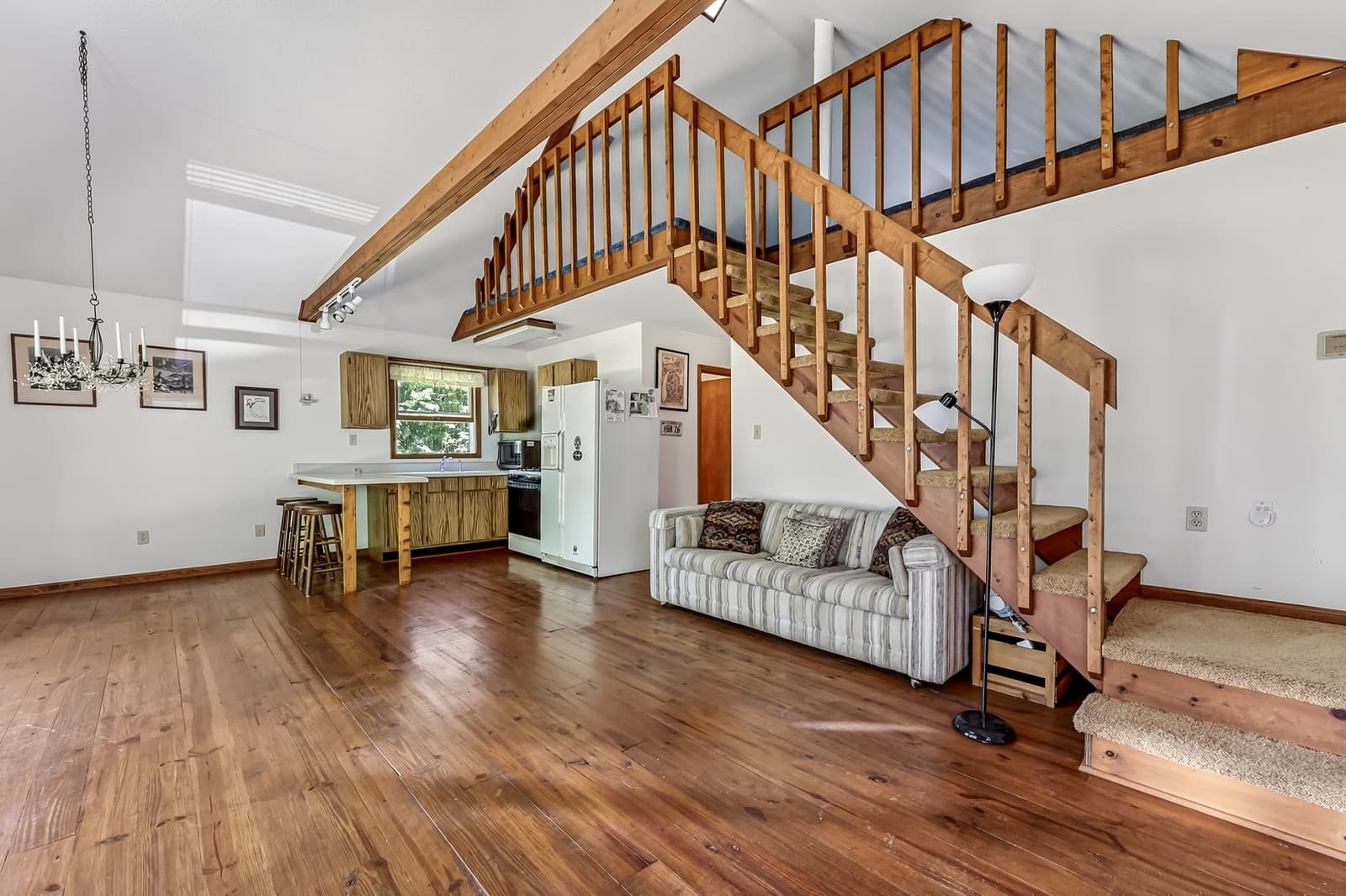 Open great room with wide pine floors, an exposed beam and a staircase up to a loft