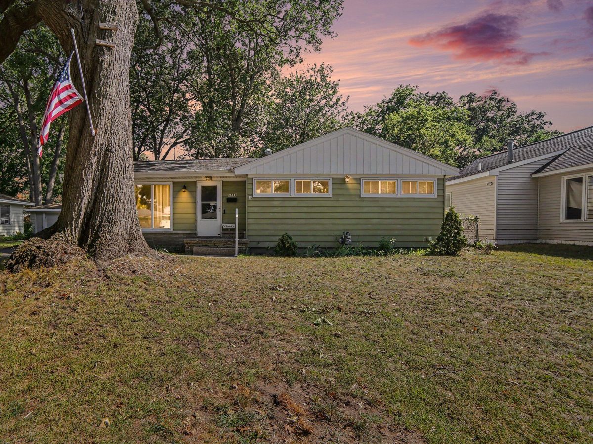 Green-sided ranch home at dusk under a large shade tree